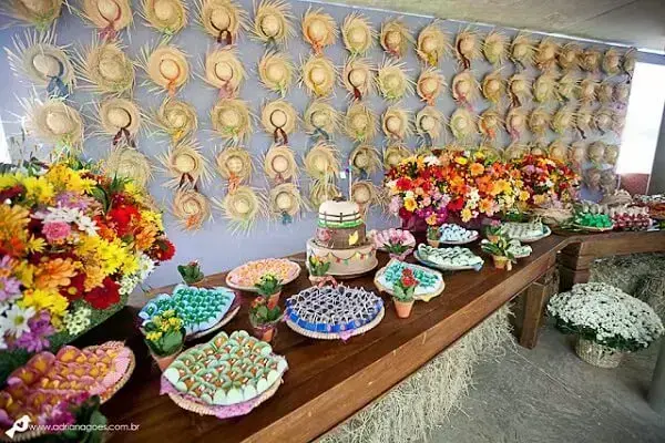 painel decorativo com chapéu de palha em evento de São João com mesa, bolo, doces e flores