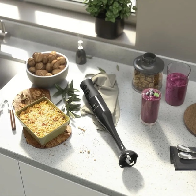 Mixer em bancada de cozinha ao lado de copos de suco e travessa com receita gratinada