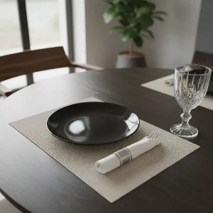 Mesa posta com jogo americano bege, guardanapo de tecido branco enrolado ao lado de prato preto.