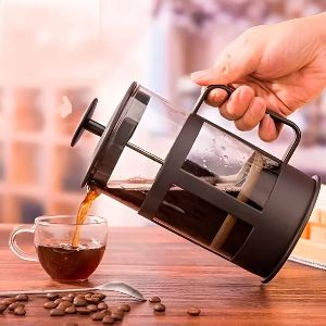 Mão feminina servindo xícara de café usando prensa francesa de vidro.