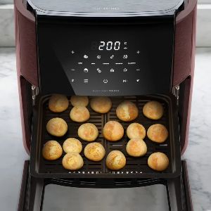 Air fyer nas cores vermelho escuro e preto, com pães de queijo assados dentro.