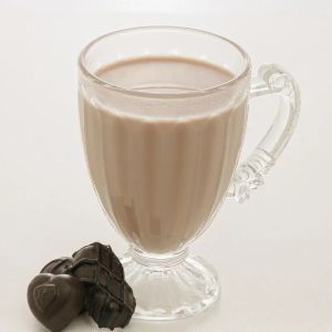 Foto de uma taça de vidro com bebida marrom dentro e bombons em formato de coração em frente.