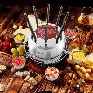 Mesa posta com panela de fondue de chocolate com potes de frutas no entorno.