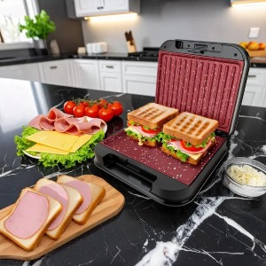 Grill elétrico em cima de bancada de cozinha com dois sanduíches dentro e ingredientes ao lado e na frente.