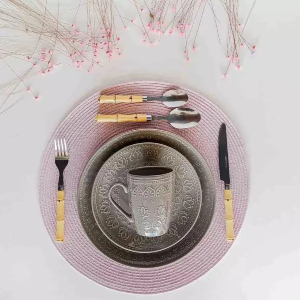 Mesa posta com pratos cinzas e caneca, com talheres com haste que reproduz bambu dos lados.